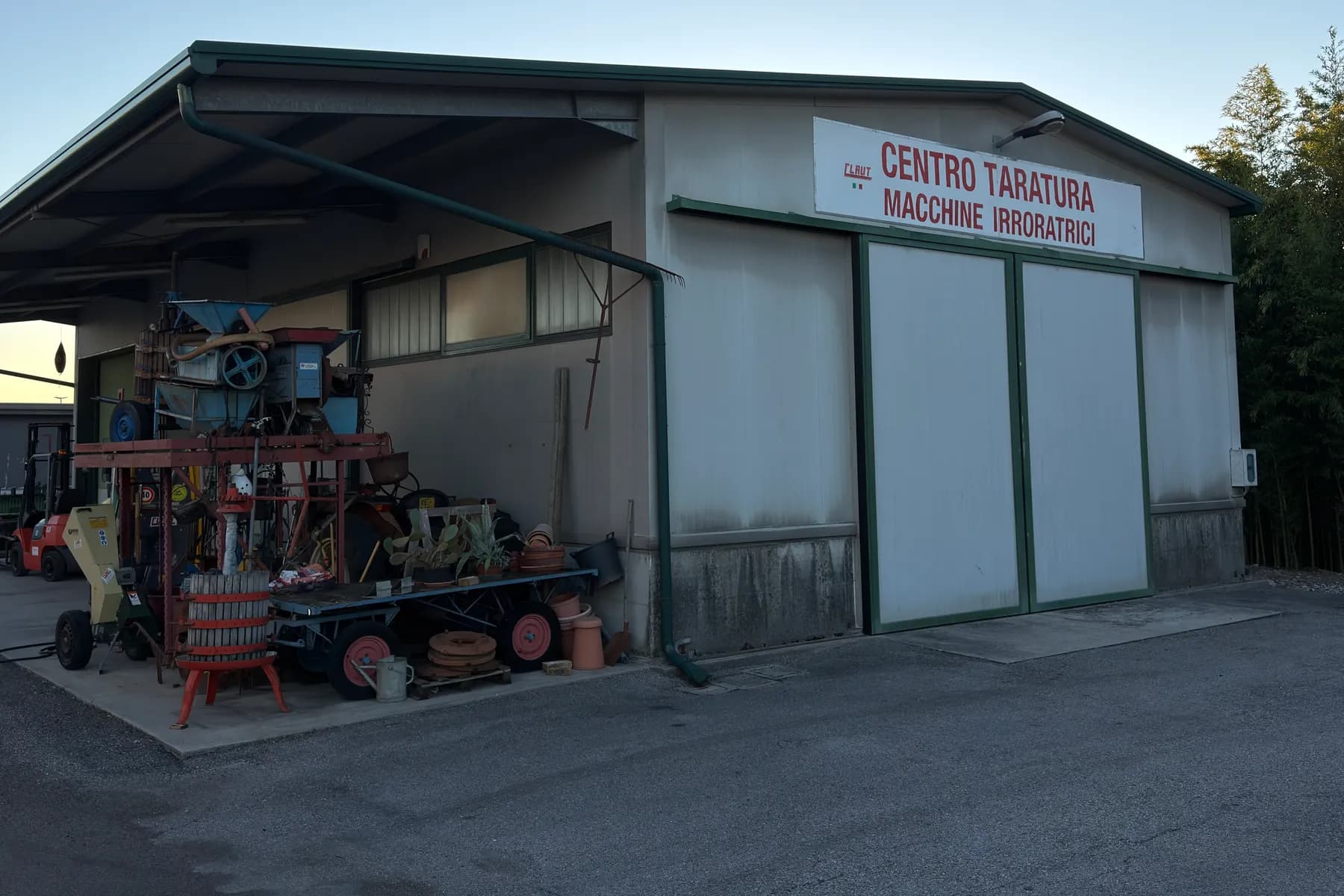 Il capannone del centro taratura macchine irroratrici di Claut, con l'insegna sopra il portone scorrevole chiuso e, a sinistra sotto la tettoia, vecchie macchine agricole